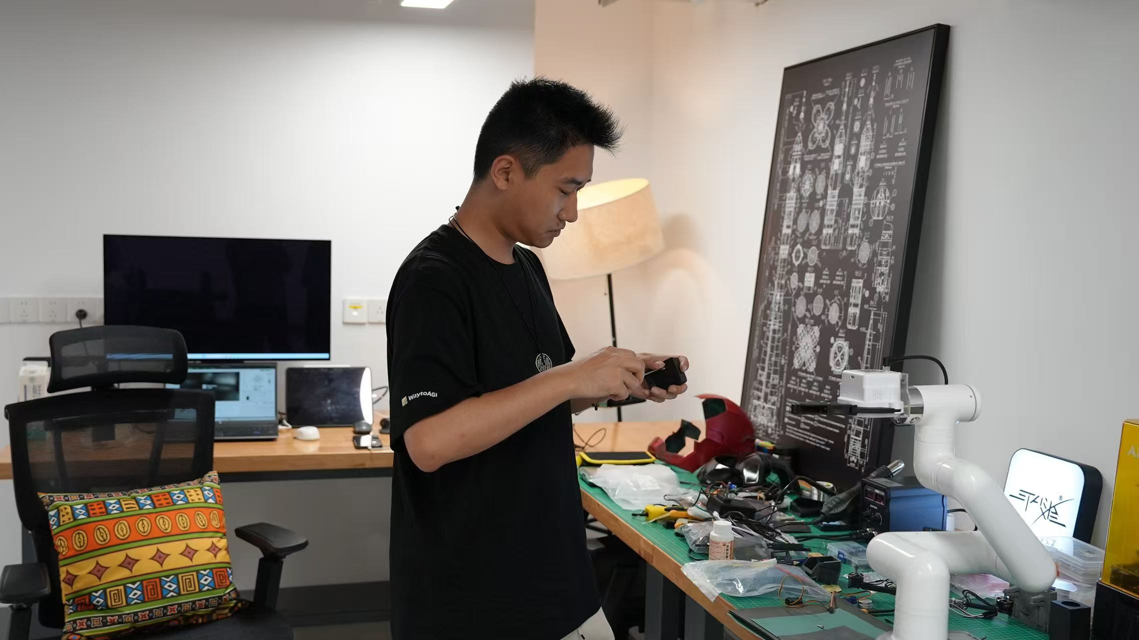 A builder working beside a robotic arm at a hardware workbench