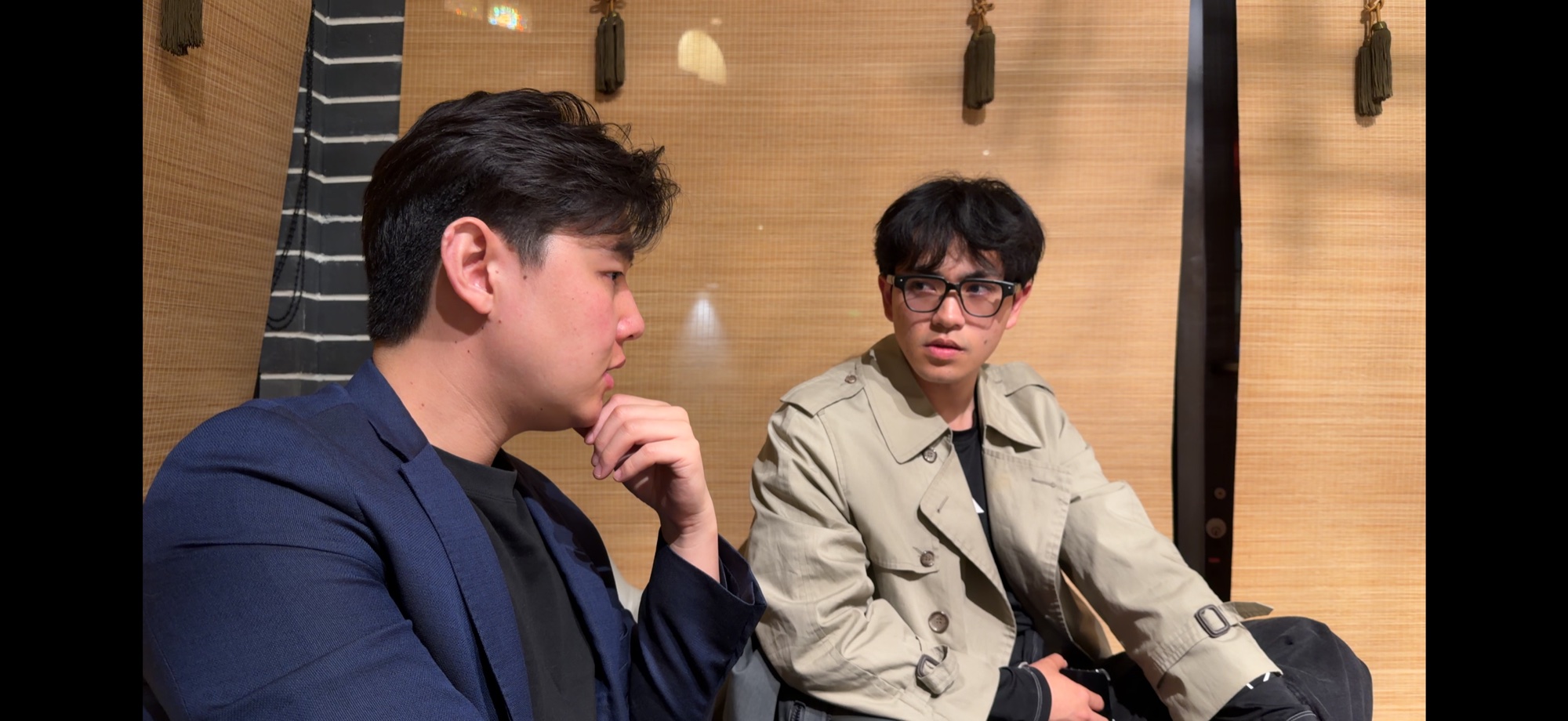 Two people in conversation beside a bamboo screen